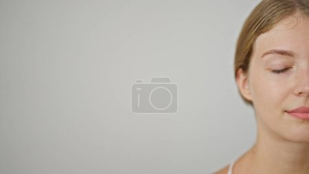 Téléchargez les photos : Jeune femme blonde debout avec un visage sérieux et les yeux fermés sur fond blanc isolé - en image libre de droit