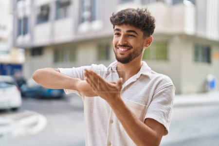 Téléchargez les photos : Jeune homme arabe souriant confiant faire dépenser de l'argent geste à la rue - en image libre de droit