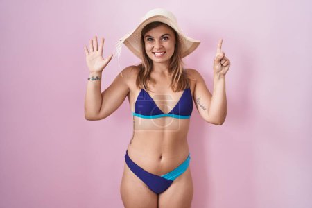 Foto de Mujer hispana joven vistiendo bikini sobre fondo rosa mostrando y señalando hacia arriba con los dedos número seis mientras sonríe confiado y feliz. - Imagen libre de derechos