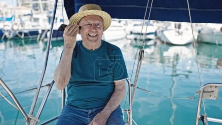 Téléchargez les photos : Homme âgé aux cheveux gris touriste portant un chapeau d'été écoutant un message vocal par smartphone au bateau - en image libre de droit