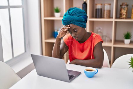 Foto de Young african american woman worried using laptop drinking coffee at home - Imagen libre de derechos
