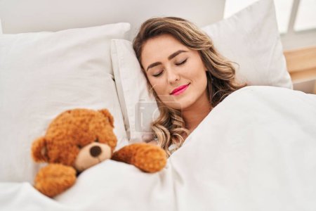 Photo for Young woman lying on bed sleeping with teddy bear at bedroom - Royalty Free Image