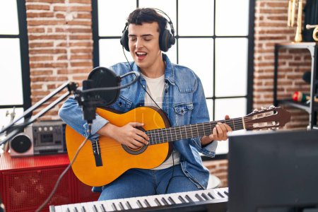Foto de Joven músico no binario cantando canción tocando guitarra clásica en el estudio de música - Imagen libre de derechos