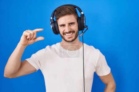Photo for Hispanic man with beard listening to music wearing headphones smiling and confident gesturing with hand doing small size sign with fingers looking and the camera. measure concept. - Royalty Free Image