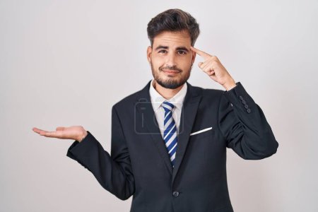 Photo for Young hispanic man with tattoos wearing business suit and tie confused and annoyed with open palm showing copy space and pointing finger to forehead. think about it. - Royalty Free Image