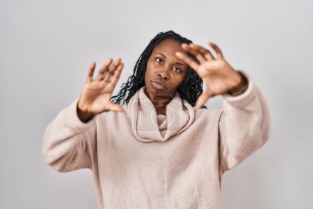 Téléchargez les photos : Femme africaine debout sur fond blanc faisant cadre en utilisant les mains paumes et les doigts, perspective de la caméra - en image libre de droit