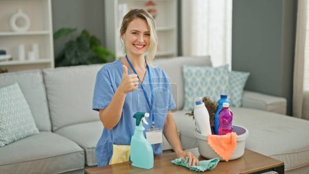 Téléchargez les photos : Jeune femme blonde nettoyage professionnel table faisant pouce geste à la maison - en image libre de droit
