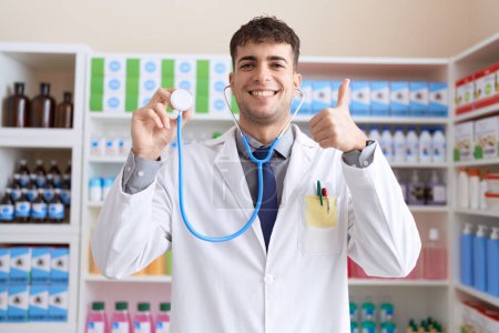 Photo for Young hispanic man wearing doctor uniform and stethoscope smiling happy and positive, thumb up doing excellent and approval sign - Royalty Free Image