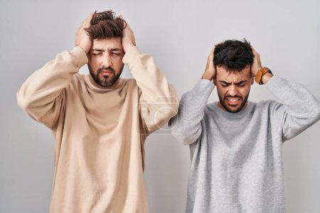 Photo for Young homosexual couple standing over white background suffering from headache desperate and stressed because pain and migraine. hands on head. - Royalty Free Image