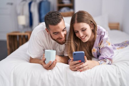 Téléchargez les photos : Homme et femme couple boire du café en utilisant un smartphone dans la chambre - en image libre de droit