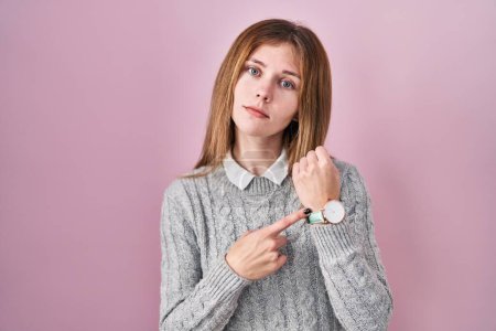Photo for Beautiful woman standing over pink background in hurry pointing to watch time, impatience, looking at the camera with relaxed expression - Royalty Free Image