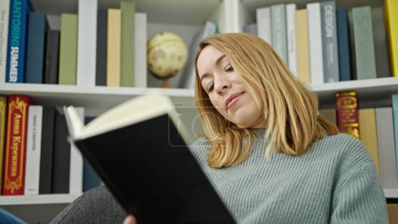Téléchargez les photos : Young blonde woman student reading book at library university - en image libre de droit