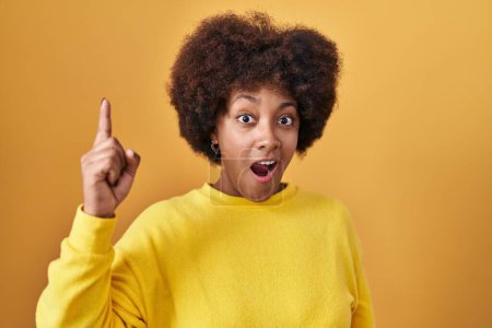 Foto de Joven mujer afroamericana de pie sobre fondo amarillo apuntando con el dedo hacia arriba con una idea exitosa. exitado y feliz. número uno. - Imagen libre de derechos