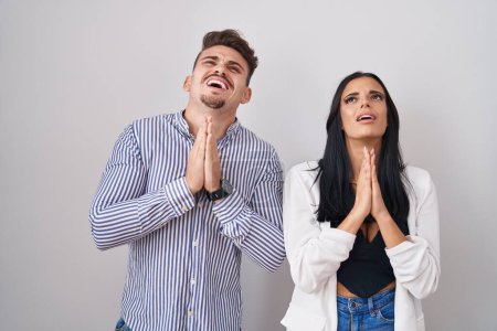 Photo for Young hispanic couple standing over white background begging and praying with hands together with hope expression on face very emotional and worried. begging. - Royalty Free Image