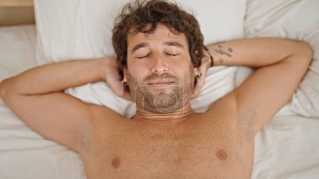Téléchargez les photos : Jeune homme hispanique détendu sur le lit torse nu dans la chambre - en image libre de droit