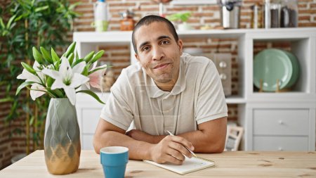 Photo for Young hispanic man sitting on table smiling at dinning room - Royalty Free Image