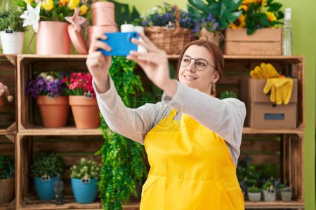 Téléchargez les photos : Jeune belle plus la taille femme fleuriste faire selfie par smartphone à la boutique de fleurs - en image libre de droit