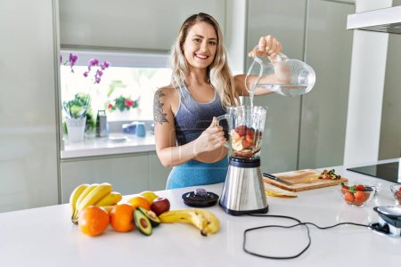 Téléchargez les photos : Young woman smiling confident pouring water on blender at kitchen - en image libre de droit