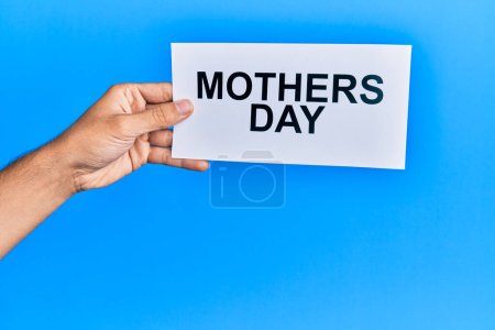 Photo for Hand of caucasian man holding paper with mothers day message over isolated blue background - Royalty Free Image