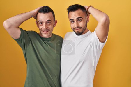 Photo for Homosexual couple standing over yellow background smiling confident touching hair with hand up gesture, posing attractive and fashionable - Royalty Free Image