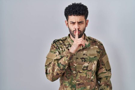 Photo for Arab man wearing camouflage army uniform asking to be quiet with finger on lips. silence and secret concept. - Royalty Free Image