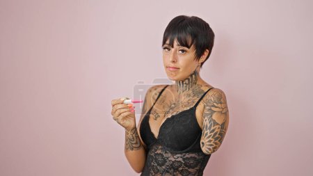 Téléchargez les photos : Femme hispanique avec bras amputé portant lingerie recherche test de grossesse sur fond rose isolé - en image libre de droit
