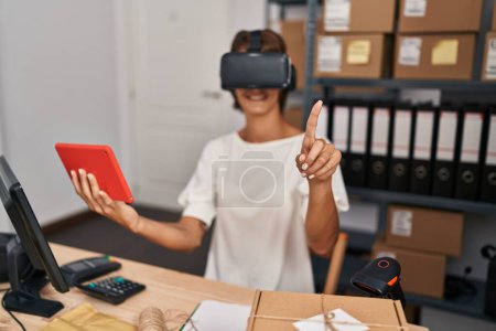 Téléchargez les photos : Jeune belle hispanique femme commerce électronique travailleur d'affaires en utilisant des lunettes de réalité virtuelle et pavé tactile au bureau - en image libre de droit