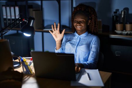 Téléchargez les photos : Femme africaine travaillant au bureau la nuit montrant et pointant du doigt le numéro cinq tout en souriant confiant et heureux. - en image libre de droit