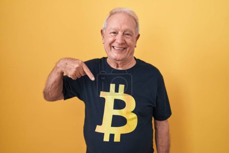 Téléchargez les photos : Homme âgé avec les cheveux gris portant Bitcoin t-shirt regardant confiant avec sourire sur le visage, se pointant avec les doigts fiers et heureux. - en image libre de droit