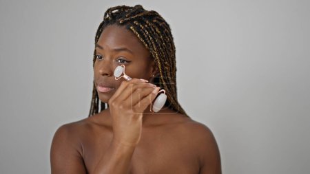 Téléchargez les photos : Femme afro-américaine massant le visage avec gymnase de la peau sur fond blanc isolé - en image libre de droit