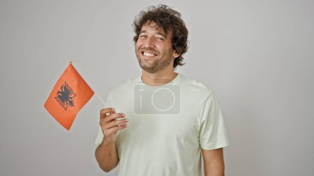 Foto de Joven hombre hispano sonriendo confiado sosteniendo bandera albanesa sobre fondo blanco aislado - Imagen libre de derechos