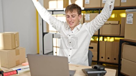 Téléchargez les photos : Jeune homme caucasien ecommerce travailleur d'affaires en utilisant un ordinateur portable avec expression gagnante au bureau - en image libre de droit