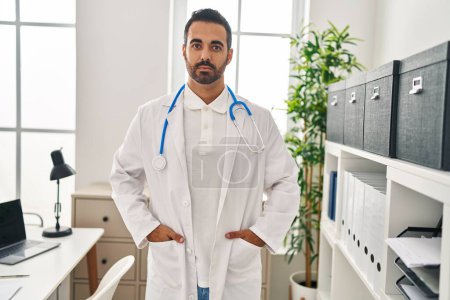 Téléchargez les photos : Young hispanic man wearing doctor uniform standing at clinic - en image libre de droit
