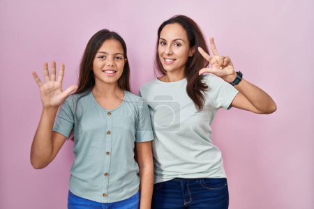 Foto de Joven madre e hija de pie sobre fondo rosa mostrando y señalando hacia arriba con los dedos número ocho mientras sonríe confiado y feliz. - Imagen libre de derechos
