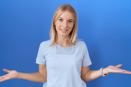 Foto de Mujer caucásica joven usando casual camiseta azul despistado y confundido con los brazos abiertos, sin concepto de idea. - Imagen libre de derechos