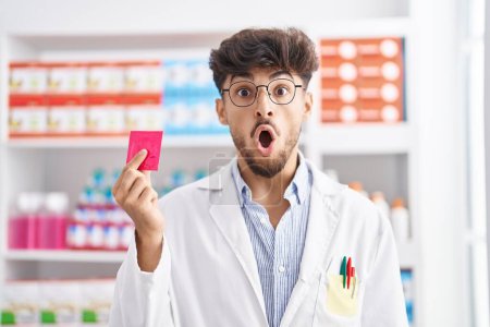 Téléchargez les photos : Homme arabe avec barbe travaillant à la pharmacie pharmacie tenant préservatif souriant avec un sourire heureux et cool sur le visage. montrant les dents. - en image libre de droit