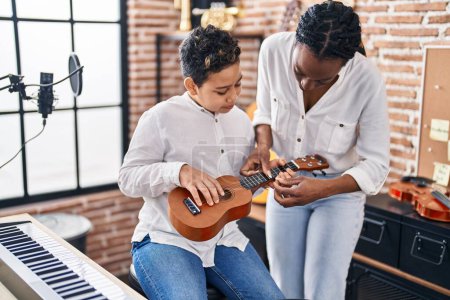 Téléchargez les photos : Afro-américaine mère et fils étudiant apprentissage jouer ukelele au studio de musique - en image libre de droit