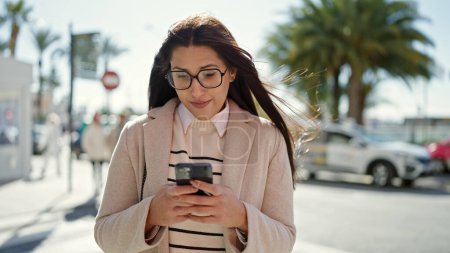 Foto de Mujer hispana hermosa joven usando teléfono inteligente con expresión seria en la calle - Imagen libre de derechos