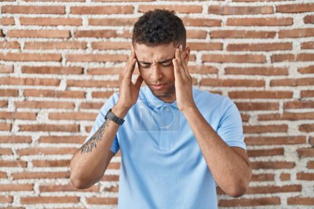 Photo for Brazilian young man standing over brick wall with hand on head, headache because stress. suffering migraine. - Royalty Free Image