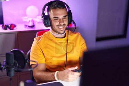 Photo for Young hispanic man streamer playing video game using joystick at gaming room - Royalty Free Image