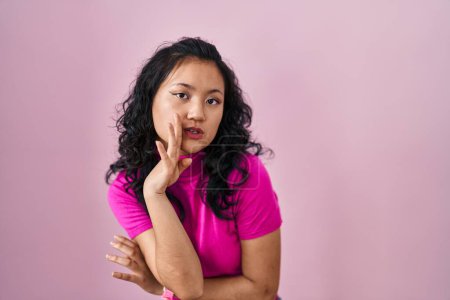 Photo for Young asian woman standing over pink background hand on mouth telling secret rumor, whispering malicious talk conversation - Royalty Free Image
