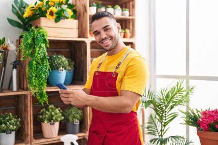Photo for Young hispanic man florist smiling confident using smartphone at florist - Royalty Free Image