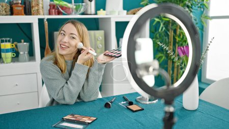 Téléchargez les photos : Jeune femme blonde enregistrement maquillage tutoriel vidéo assis sur la table à manger salle - en image libre de droit