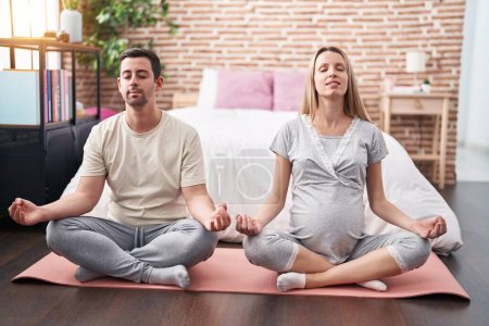Foto de Hombre y mujer pareja esperando vientre haciendo ejercicio de yoga en el dormitorio - Imagen libre de derechos