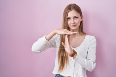 Photo for Young caucasian woman standing over pink background doing time out gesture with hands, frustrated and serious face - Royalty Free Image