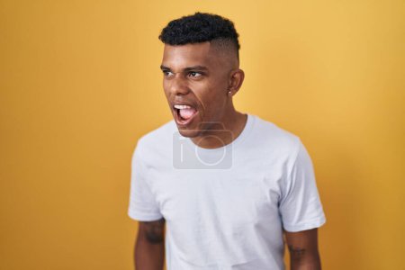 Photo for Young hispanic man standing over yellow background angry and mad screaming frustrated and furious, shouting with anger. rage and aggressive concept. - Royalty Free Image