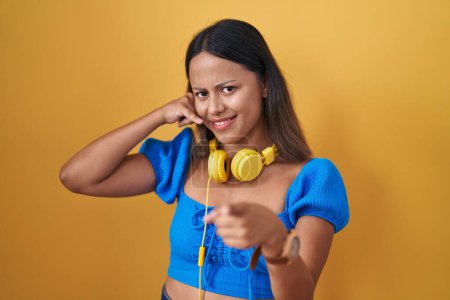 Téléchargez les photos : Jeune femme hispanique debout sur fond jaune souriant faire parler au téléphone geste et vous pointant du doigt. Appelle-moi. - en image libre de droit