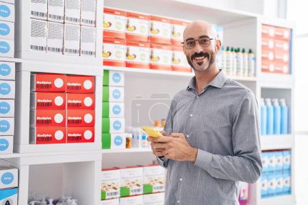 Photo for Young hispanic man customer smiling confident using smartphone at pharmacy - Royalty Free Image