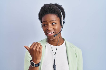 Téléchargez les photos : Femme afro-américaine portant casque agent du centre d'appel souriant avec le visage heureux regardant et pointant vers le côté avec le pouce vers le haut. - en image libre de droit