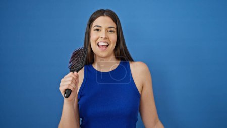 Téléchargez les photos : Jeune belle femme hispanique chantant chanson à l'aide d'un pinceau comme un microphone sur fond bleu isolé - en image libre de droit